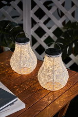 Two white plastic solar lanterns with intricate pattern on wooden table, outdoor garden lighting