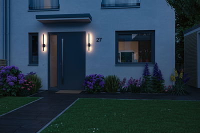 Moderne hus med mørkeblå dør og to slanke sorte udendørs væglamper ved skumring