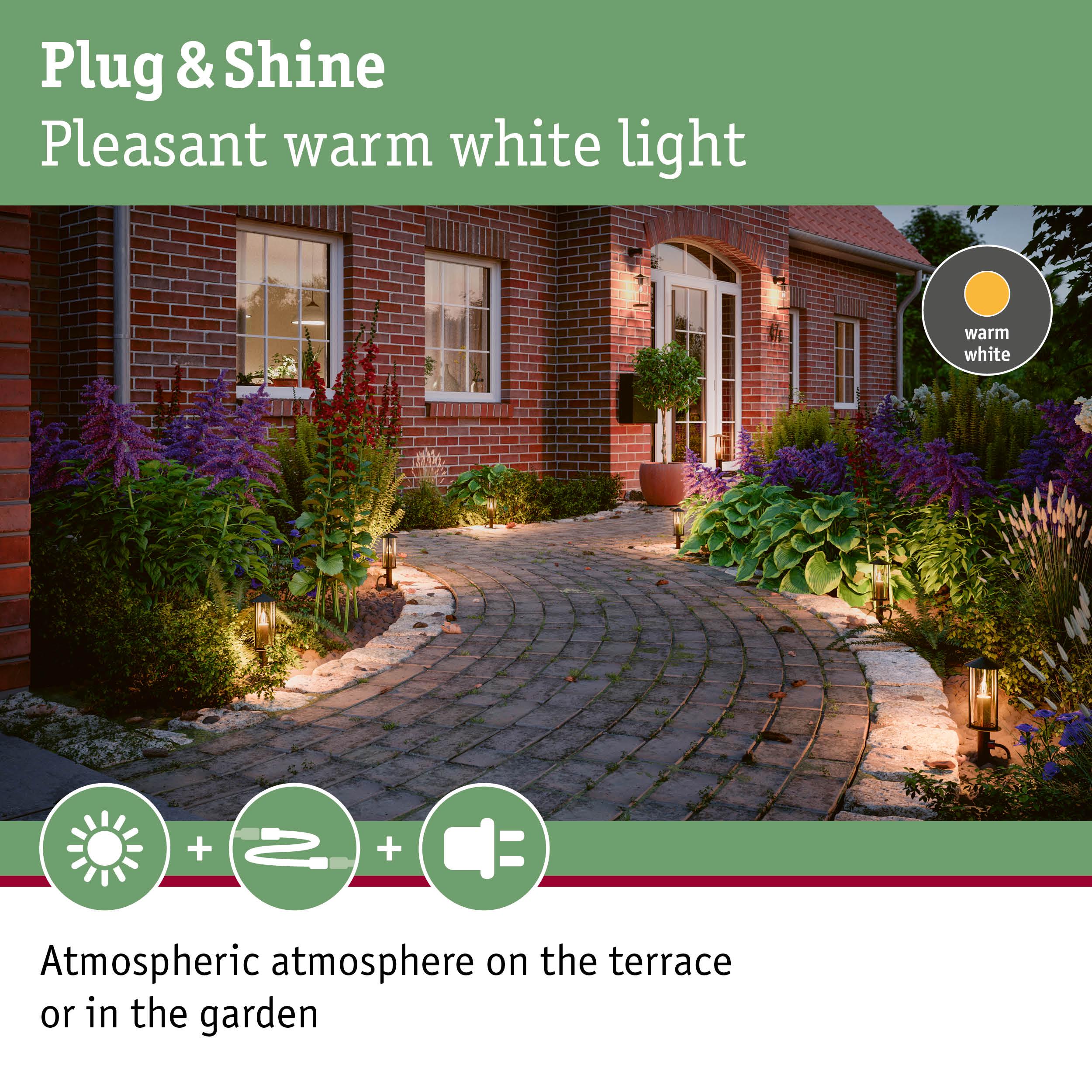 Warm white garden path lights along brick house creating atmospheric terrace and garden lighting