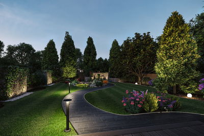 Modern garden path with black paving and metal LED bollard lights in green area at dusk
