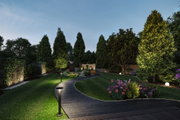 Moderner Gartenweg mit schwarzer Pflasterung und LED-Wegeleuchten aus Metall in Grünanlage bei Abendlicht