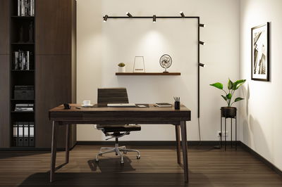 Bureau moderne avec bureau en bois foncé, chaise en cuir noir et lampe murale LED noire pour éclairage.