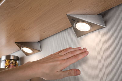 Triangular brushed stainless steel LED under-cabinet lights with warm white light on wood surface.