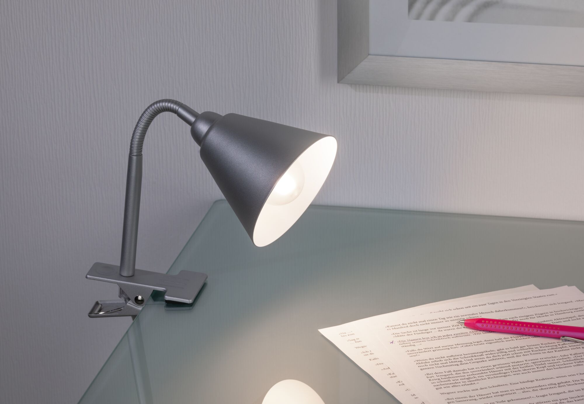 Moderner grauer Metall-Klemmspot mit flexiblem Hals auf Glas-Schreibtisch mit Papier und Stift