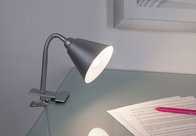 Moderner grauer Metall-Klemmspot mit flexiblem Hals auf Glas-Schreibtisch mit Papier und Stift