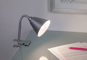 Moderner grauer Metall-Klemmspot mit flexiblem Hals auf Glas-Schreibtisch mit Papier und Stift