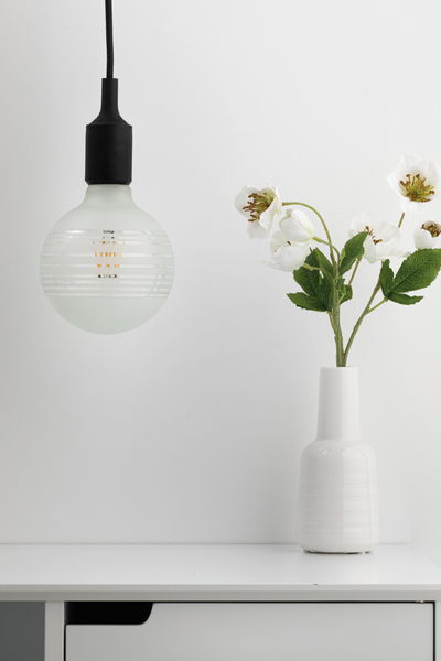 Moderne hanglamp met matglas en zwarte details boven wit dressoir met vaas en witte bloemen