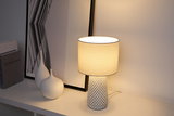 Lampe de table avec abat-jour en tissu blanc et base en céramique à motif sur meuble blanc.