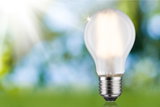Glowing LED light bulb with clear glass and metal base against green-blue blurred background