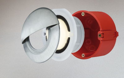 Exploded view of round LED recessed light with brushed stainless steel and red plastic housing.