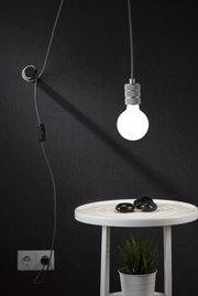 Hängende Glühbirne mit grauem Metallfassung und schwarzem Kabel vor dunklem Hintergrund, moderne Beleuchtung