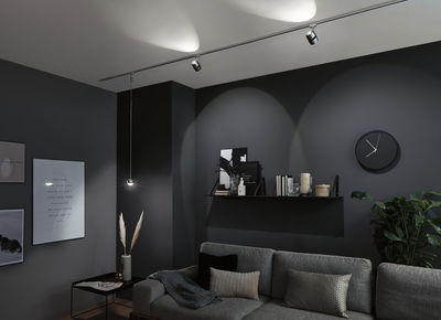 Salon moderne avec canapé gris, horloge murale noire et éclairage LED sur rail minimaliste.