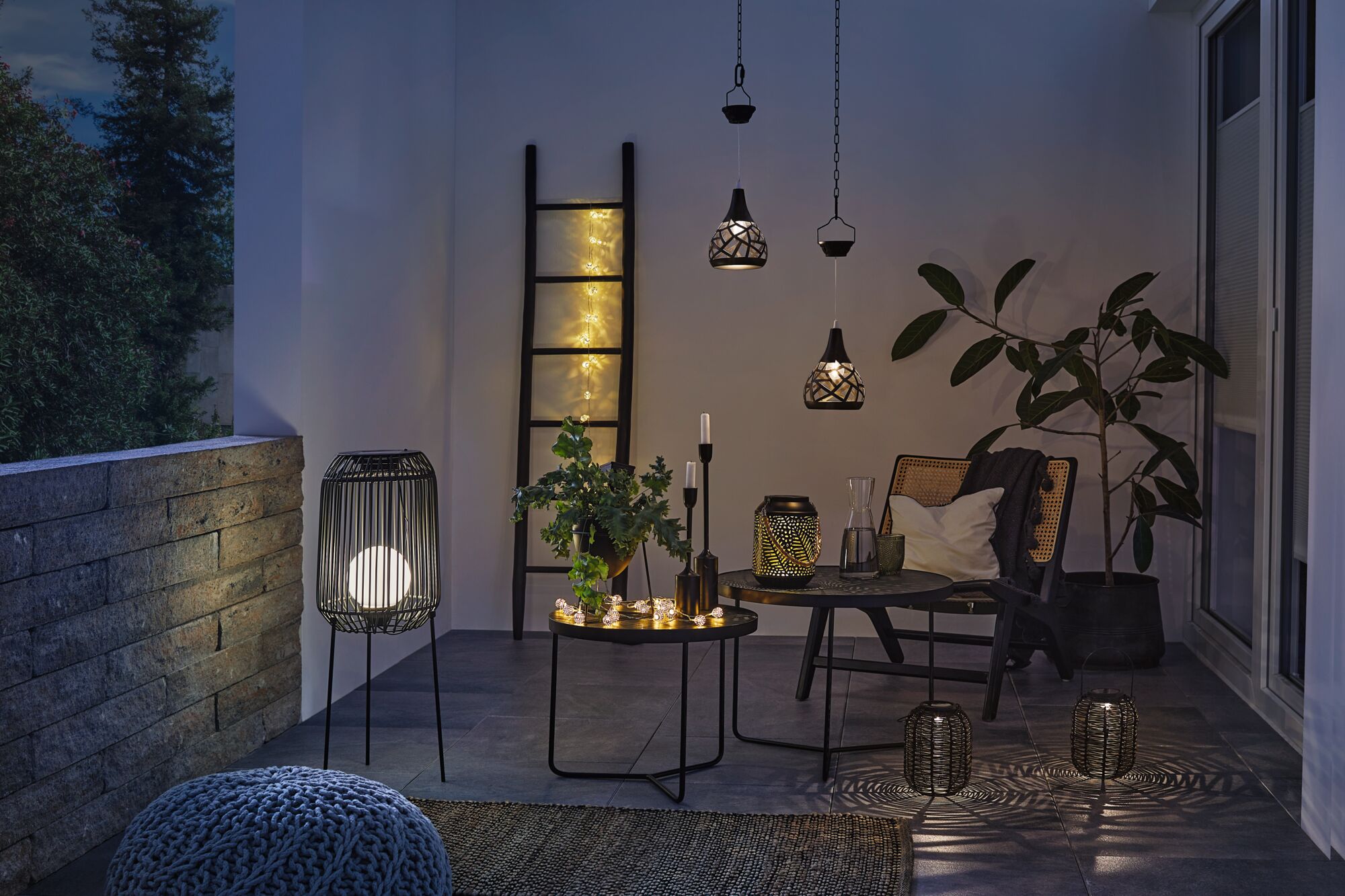 Gezellig terras met zwarte metalen lampen, LED-lichtsnoer en planten voor sfeervolle buitenverlichting.