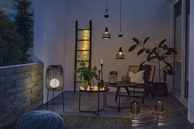 Hyggelig terrasse med sorte metallamper, LED-lyskæde og planter til stemningsfuld udendørsbelysning.
