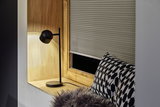 Black metal desk lamp with round head on wooden windowsill near patterned cushion and pleated blind.