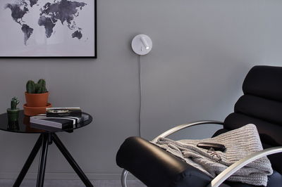 Moderner weißer LED-Wandleuchter mit rundem Sockel an grauer Wand im Wohnzimmer mit schwarzem Sessel.