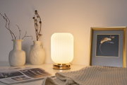 Modern white table lamp with ribbed glass and gold base beside ceramic vases and framed artwork