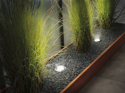 Luminaires LED encastrés en acier inoxydable éclairant des plantes vertes dans un lit de gravier avec cadre en bois