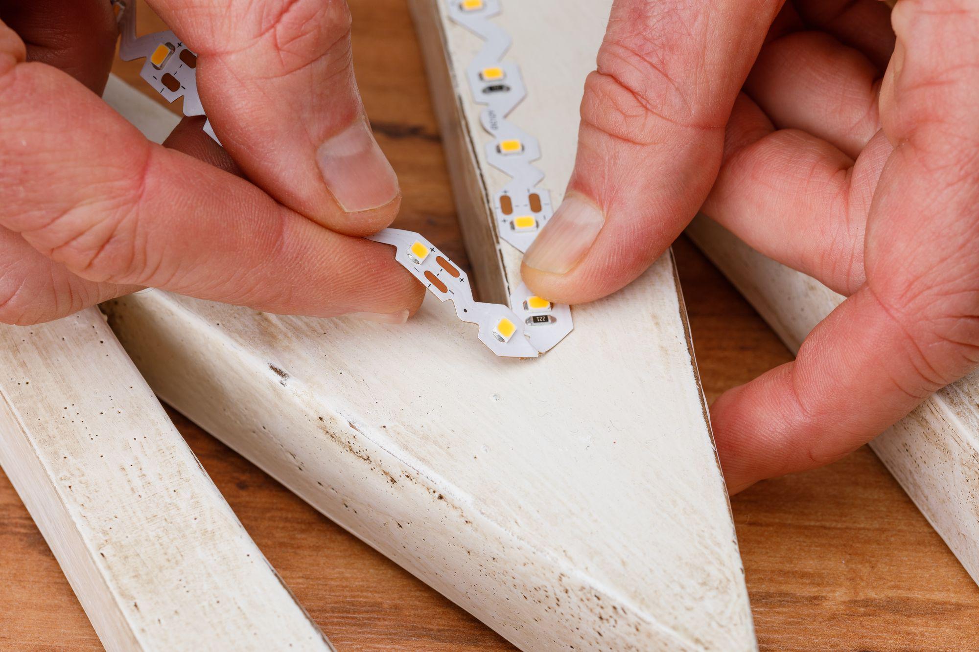 Handen plaatsen witte LED-strip met zichtbare LED-chips op wit geschilderd hout voor verlichting