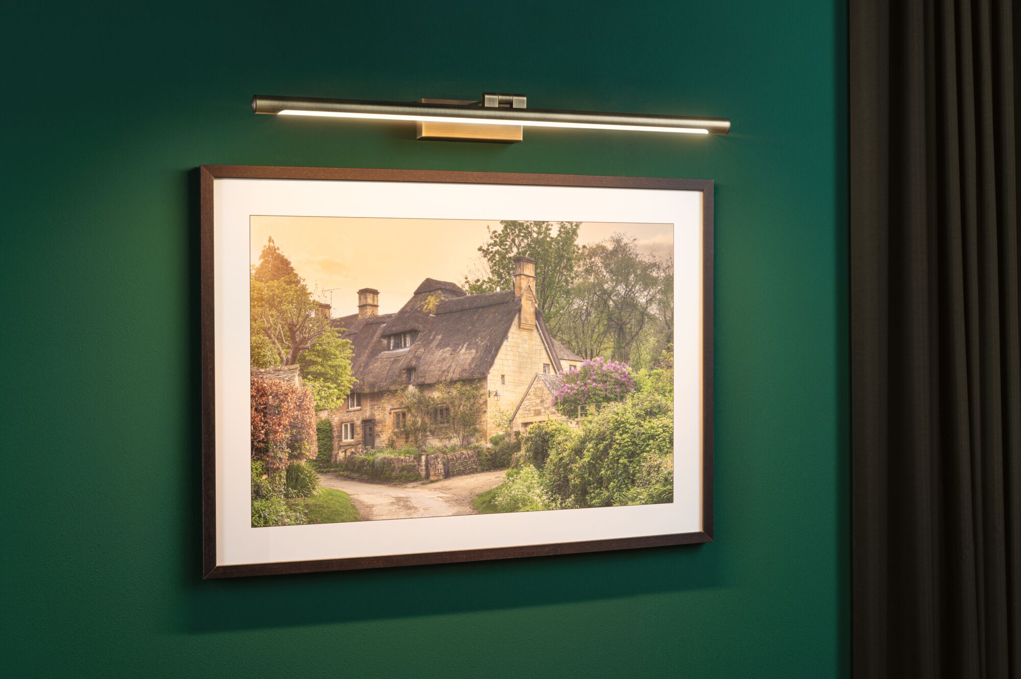 Slanke LED-kunstlicht in messingkleur aan groene muur verlicht ingelijste landschapsfoto.