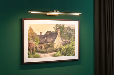 Slanke LED-kunstlicht in messingkleur aan groene muur verlicht ingelijste landschapsfoto.