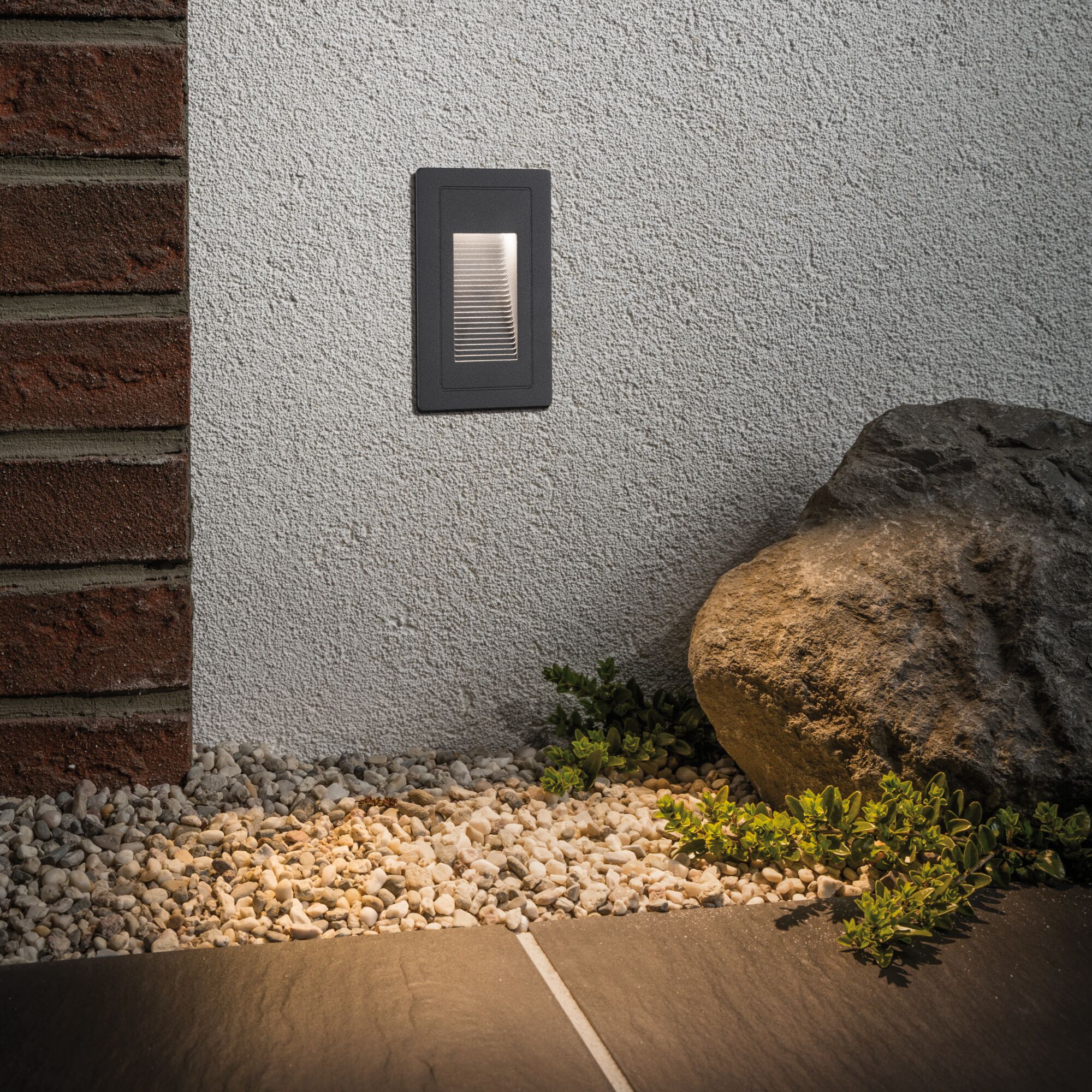 Zwarte metalen LED-wandlamp op witte muur die kiezelstenen en planten buiten verlicht