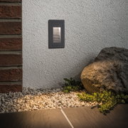 Applique murale LED noire en métal sur mur extérieur blanc avec pierres et gravier de jardin