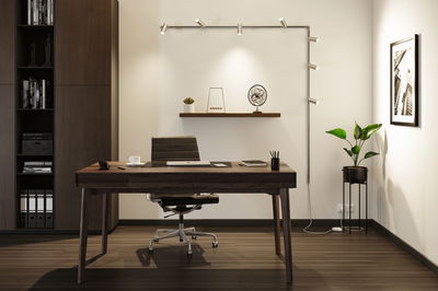 Moderne kontor med mørkt træbord, sort læderstol og minimalistisk vægbelysning