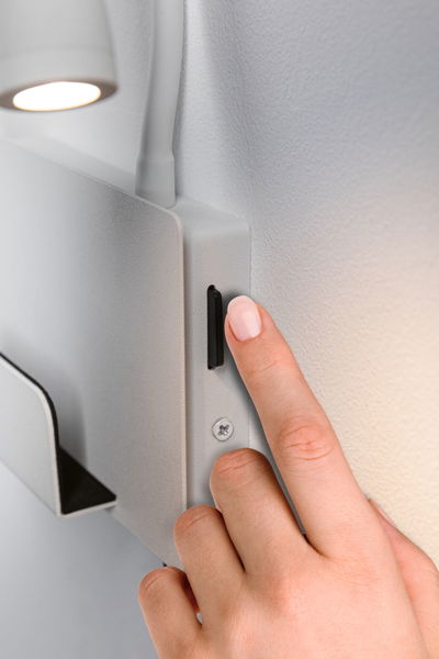 Hand pressing black switch on white metal wall lamp with LED light for indoor use