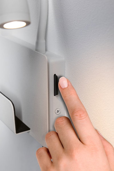 Hand pressing black switch on white metal wall lamp with LED light for indoor use