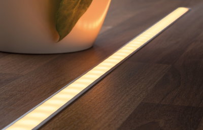Warm white LED strip light in white aluminum profile on dark wood floor for indirect lighting