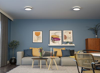 Salon moderne avec canapé gris, murs bleus et deux tables basses rondes en bois avec bougies.