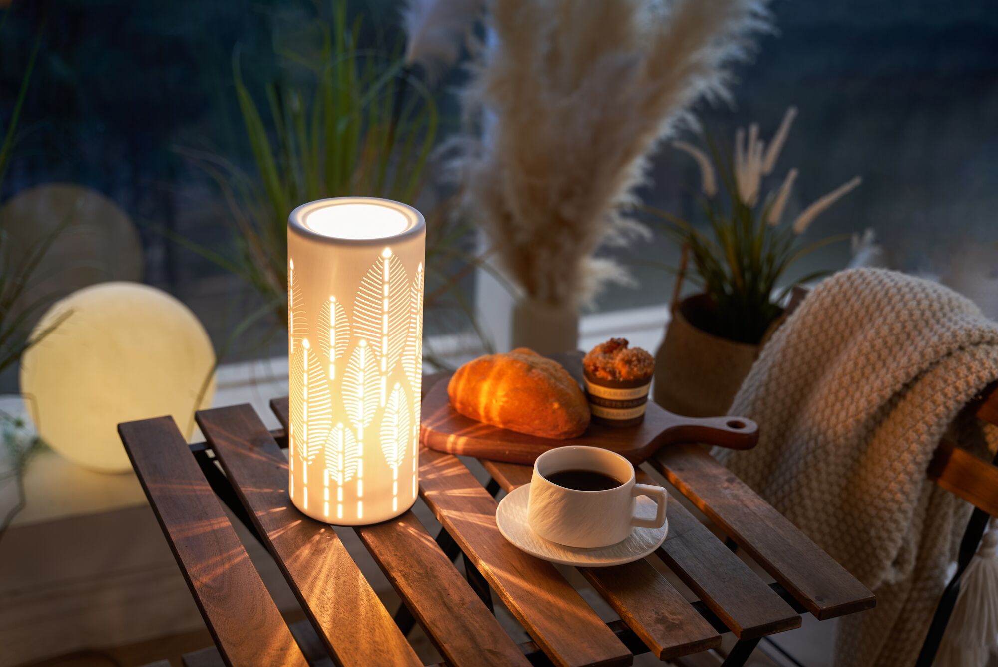 Lampe de table LED blanche en métal avec motif feuilles sur table en bois près de café et pâtisserie