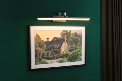 Applique LED moderne en métal avec lumière blanc chaud sur mur vert et tableau de maison.