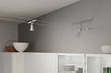 White metal cable spotlight on grey wall above white kitchen cabinet with dishes and decor.