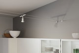 Weißer Seilstrahler aus Metall an grauer Wand über weißem Küchenschrank mit Geschirr und Dekoration.