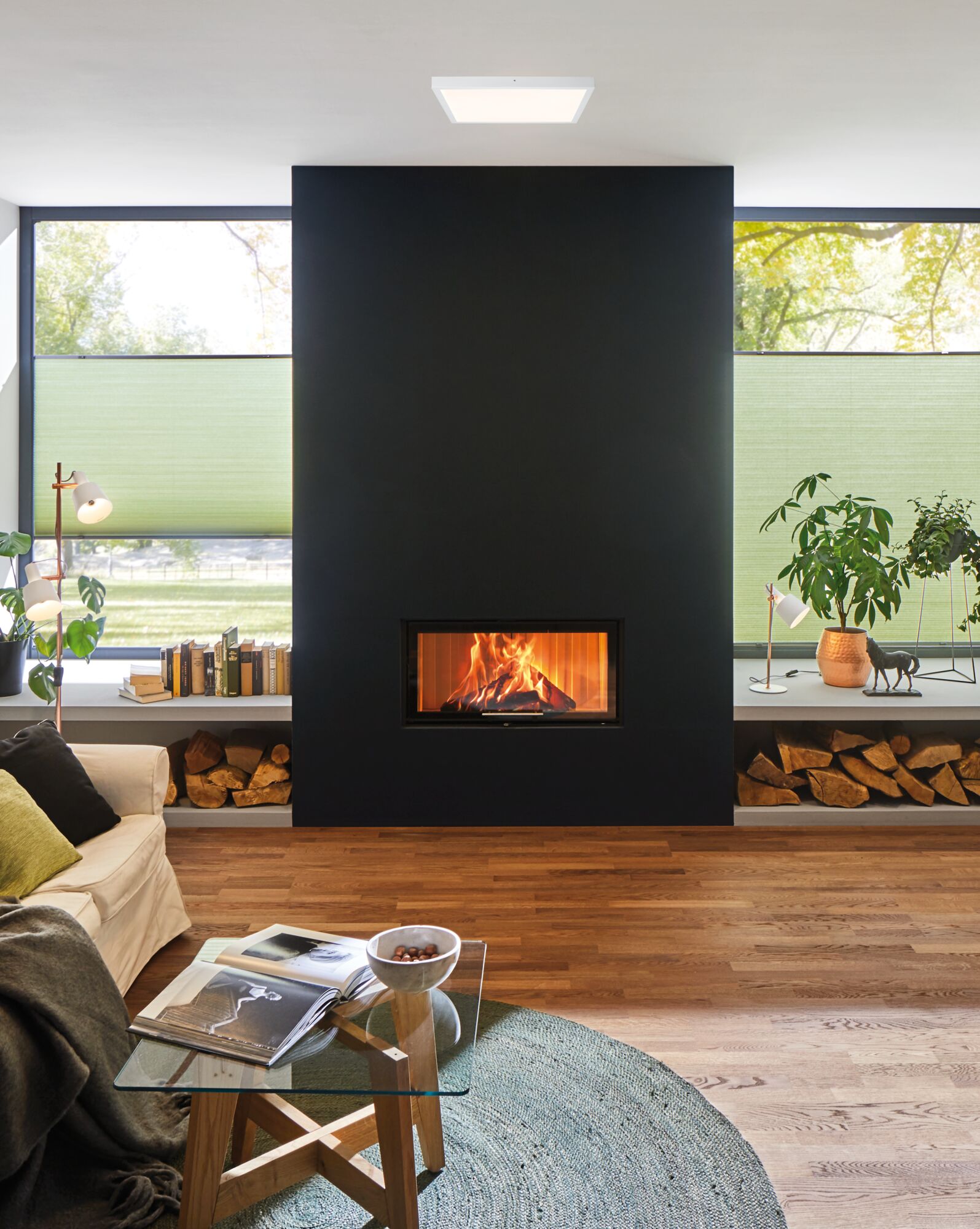 Modernes Wohnzimmer mit schwarzer Kaminwand, Holzlager und quadratischer Deckenleuchte in Weiß