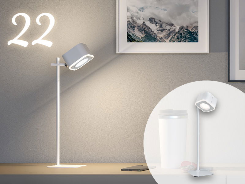 Weiße LED-Tischleuchte mit rundem Lampenkopf auf Schreibtisch vor grauer Wand mit Bilderrahmen