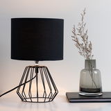 Modern table lamp with black fabric shade and geometric metal frame for stylish home lighting.