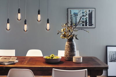 Five hanging vintage light bulbs with warm glow above wooden table with decor and white chairs