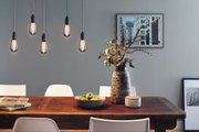Five hanging vintage light bulbs with warm glow above wooden table with decor and white chairs