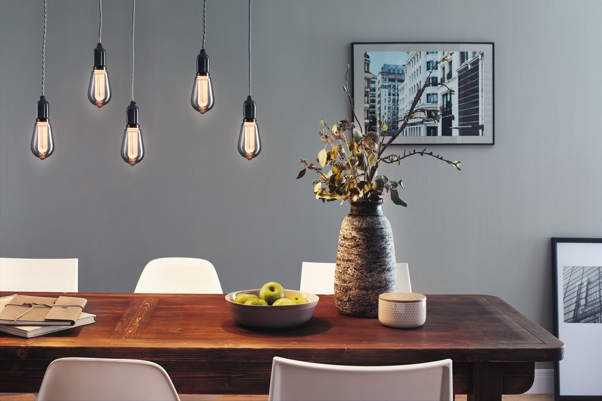Five hanging vintage light bulbs with warm glow above wooden table with decor and white chairs
