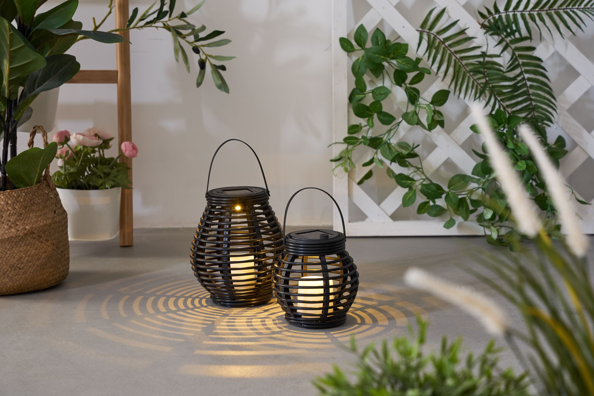 Two black metal solar lanterns with warm white LED light casting decorative shadows indoors.