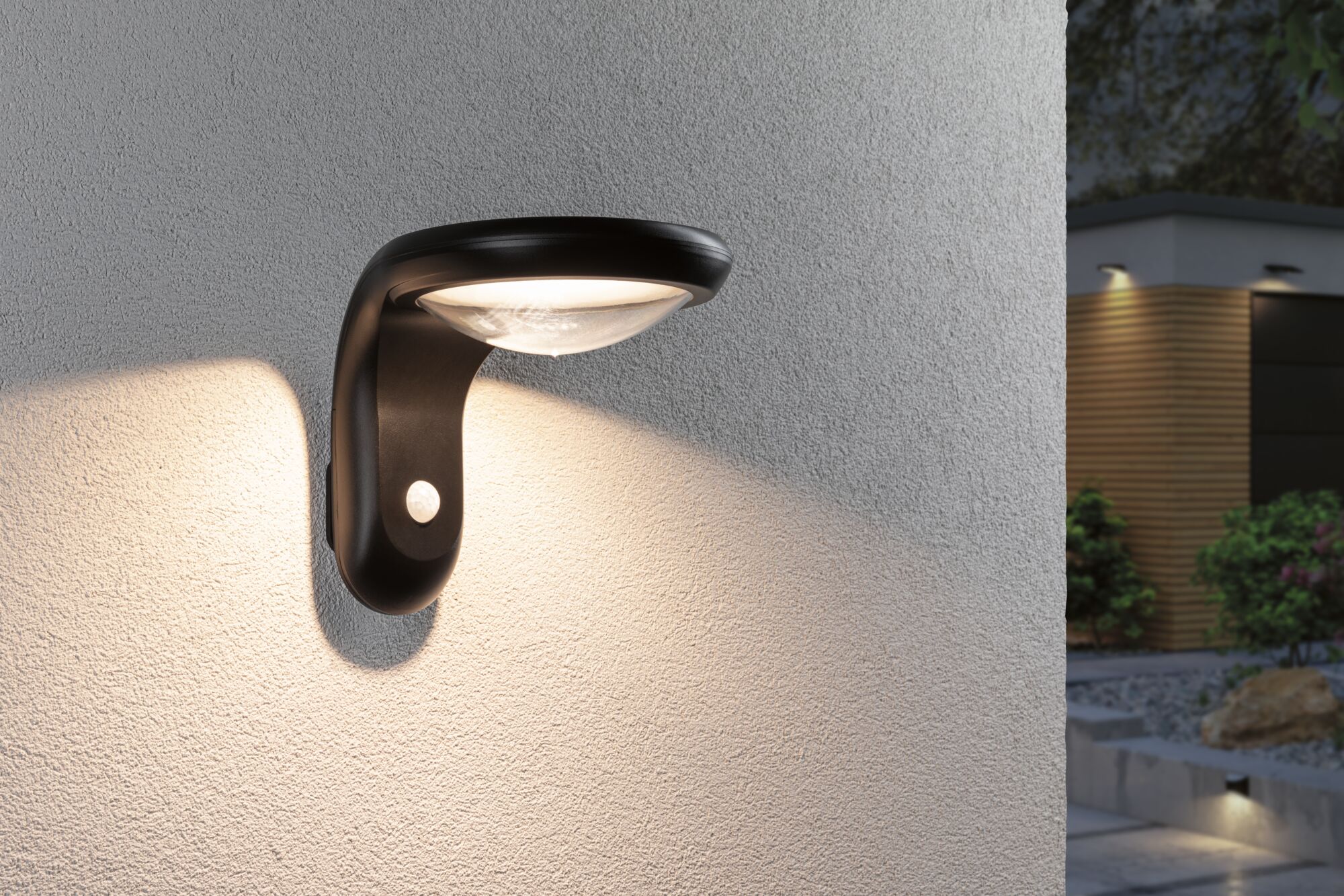 Black outdoor wall light with motion sensor illuminating house wall and garden path at night