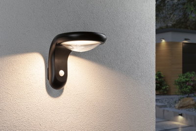 Black outdoor wall light with motion sensor illuminating house wall and garden path at night
