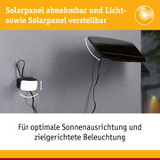 Schwarzes, verstellbares Solarpanel an grauer Wand mit angeschlossener Lampe für gezielte Beleuchtung