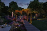 Illuminated garden path with LED recessed lights and trellis in green garden at dusk