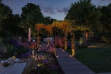 Allée de jardin éclairée avec spots LED encastrés et treillis dans un jardin vert au crépuscule