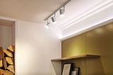 Drei weiße LED-Strahler an grauer Schiene an Decke in modernem Raum mit Holzregal und Bildern.
