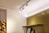 Trois spots LED blancs sur rail gris au plafond dans une pièce moderne avec étagère en bois et cadres.